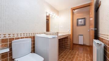A bathroom with a toilet, a washing machine, a sink, a mirror, and a radiator.