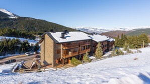 Un immeuble à plusieurs étages doté de balcons, entouré de montagnes enneigées et surplombant un ciel dégagé.