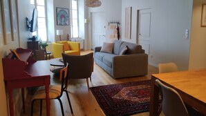 A spacious living room with a grey sofa, yellow armchairs, a red dining table, and a patterned rug. - "Le Sarment, Beaune historic district downtown (Beaune)