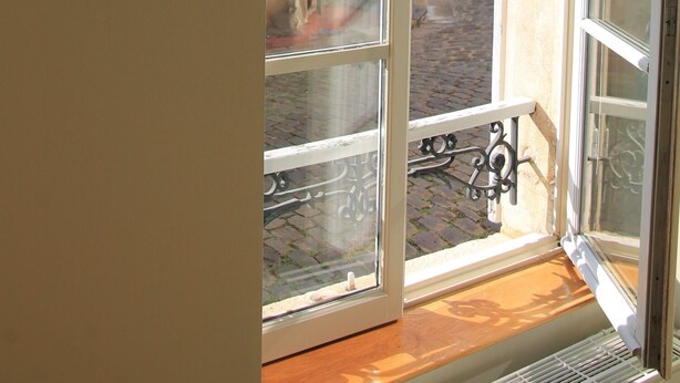 A view through a window with a metal balcony railing, looking out onto a cobblestone street with buildings. - "Le Sarment, Beaune historic district downtown (Beaune)