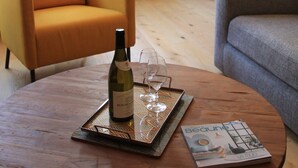 A living room with a wooden coffee table, a bottle of wine, and a magazine. There is a yellow armchair and a gray sofa. A framed picture is on the wall, and a door is visible in the background. - "Le Sarment, Beaune historic district downtown (Beaune)