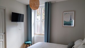 A bedroom with a bed, a television mounted on the wall, a window with curtains, and a small stool. - "Le Sarment, Beaune historic district downtown (Beaune)