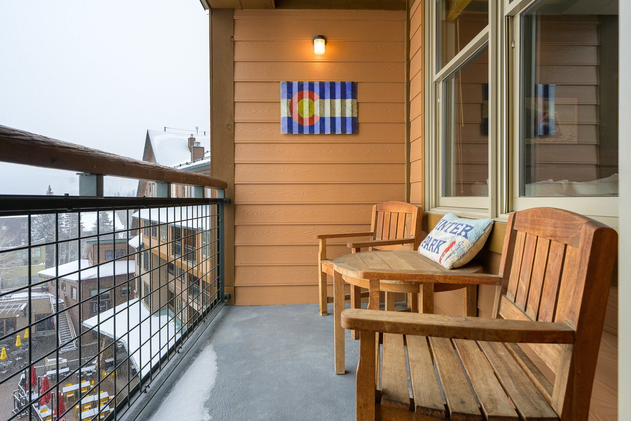 A wooden balcony with a view of the city, a wooden bench, and a wall-mounted light fixture.