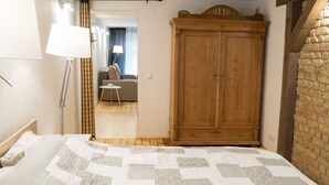 Ein Schlafzimmer mit einem Bett, einem Holzschrank, einer Lampe und Blick in einen weiteren Raum.