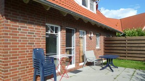 Une maison en briques avec un toit en tuiles, une terrasse avec une table et des chaises, et une clôture en bois.