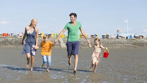 Une famille se promène sur une plage de sable, sous un ciel dégagé.