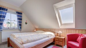 Une chambre à coucher avec un lit en bois, une chaise rouge, une fenêtre avec des rideaux et un puits de lumière.
