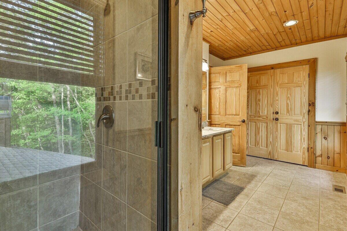 A modern bathroom with a glass shower door, wooden cabinets, and a view of the forest.