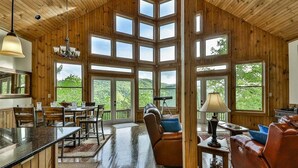 A spacious room with a high ceiling, large windows, a dining area, and a seating area with a fireplace. - Altitude Adjustment | Cherry Log, Ga (Cherry Log)