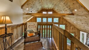 A cozy loft bedroom with a sloped ceiling, a cushioned bench, a lamp, and a view of the outdoors. - Altitude Adjustment | Cherry Log, Ga (Cherry Log)