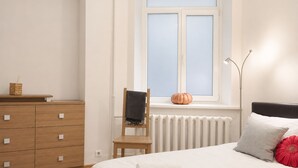 Ein Schlafzimmer mit einem Bett, einer Holzkommode, einem Sessel, einer Heizung und einem Fenster mit Blick.