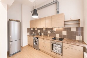 A modern kitchen with stainless steel appliances, wooden cabinets, a built-in washing machine, and a tiled backsplash.