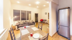Ein modernes Wohnzimmer mit Esstisch für zwei Personen, einer Couch, einem roten Sessel und einem großen Fenster.