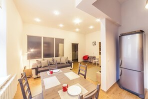 A modern living room with a dining table set for two, a sofa, a red chair, and a large window.