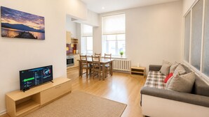 Ein modernes Wohnzimmer mit einer Couch, einem Fernseher und einem Essbereich mit Stühlen und einem Tisch.