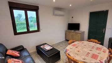 A living room with a sofa, a coffee table, a TV, a dining table with chairs, a window, and a fireplace.