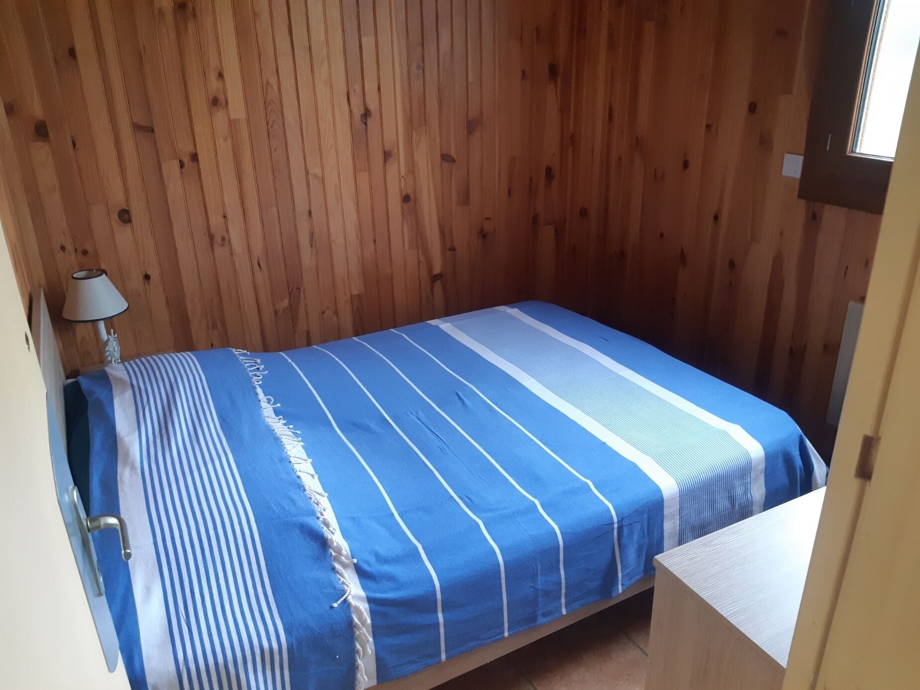 Une petite chambre avec un lit simple, un mur en bois et une fenêtre.