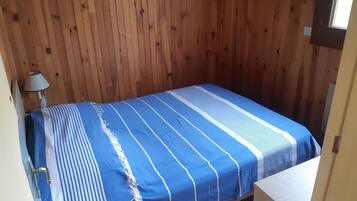 Une petite chambre avec un lit simple, un mur en bois et une fenêtre.