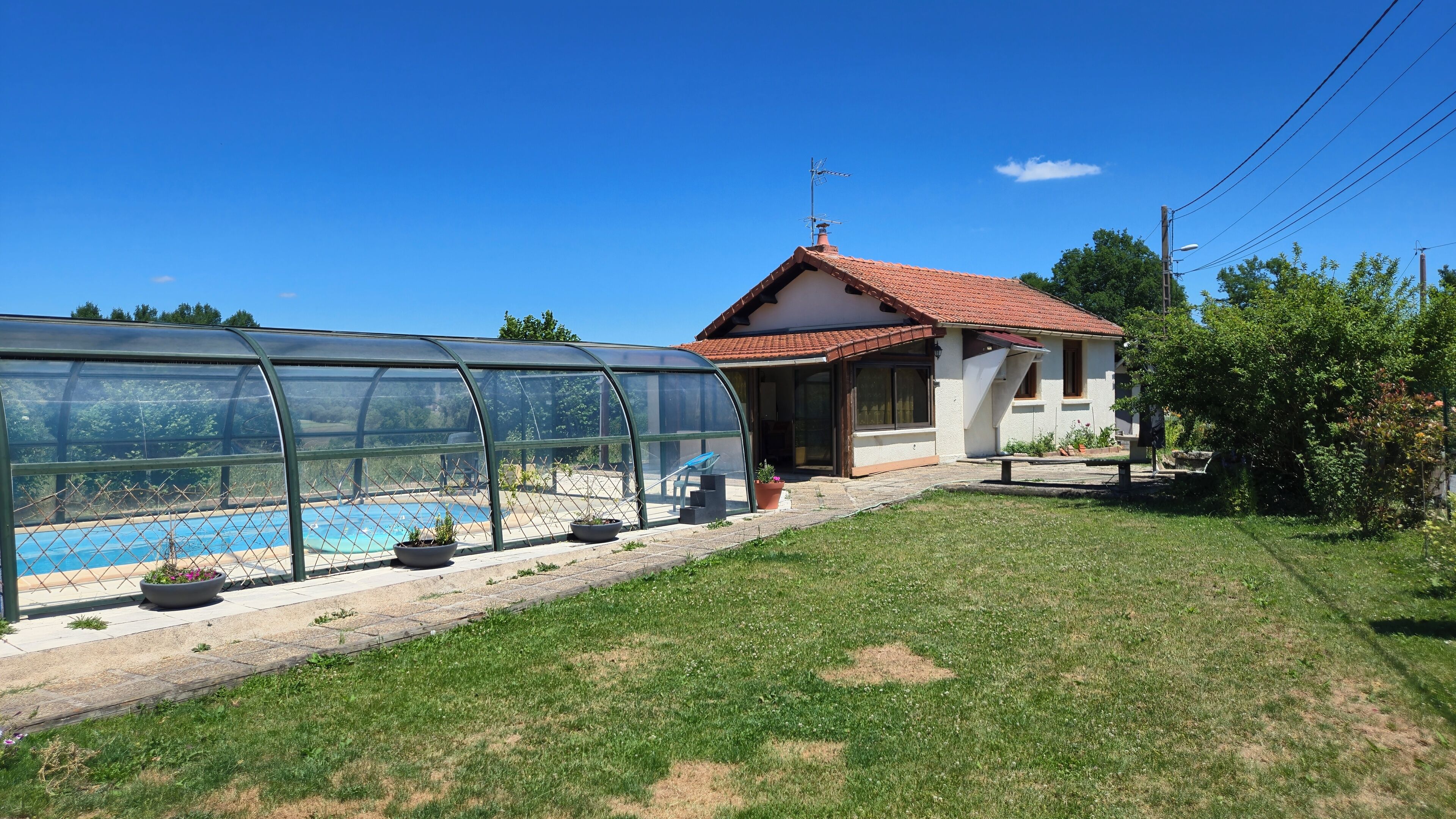 Et hus med swimmingpool, drivhus og en lille have.