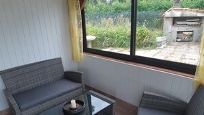 Une pièce avec un canapé gris, une table basse en verre et une vue sur un jardin par la fenêtre.