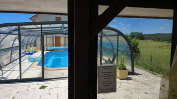 A glass-enclosed pool area with a sign indicating it is a mandatory swimming area, surrounded by a paved deck and a view of a green landscape.