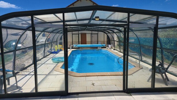 Une piscine couverte, dotée d’une structure en verre, d’un banc et d’une petite table.