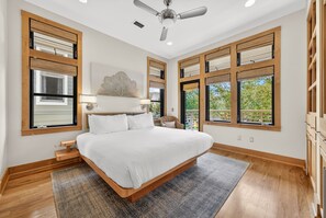 A bedroom with a large bed, wooden floor, and multiple windows.