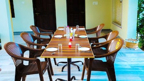 A dining area with a long table set for six, surrounded by six brown chairs with perforated backs. - Hotel Mewad Haveli Pushkar (Pushkar)