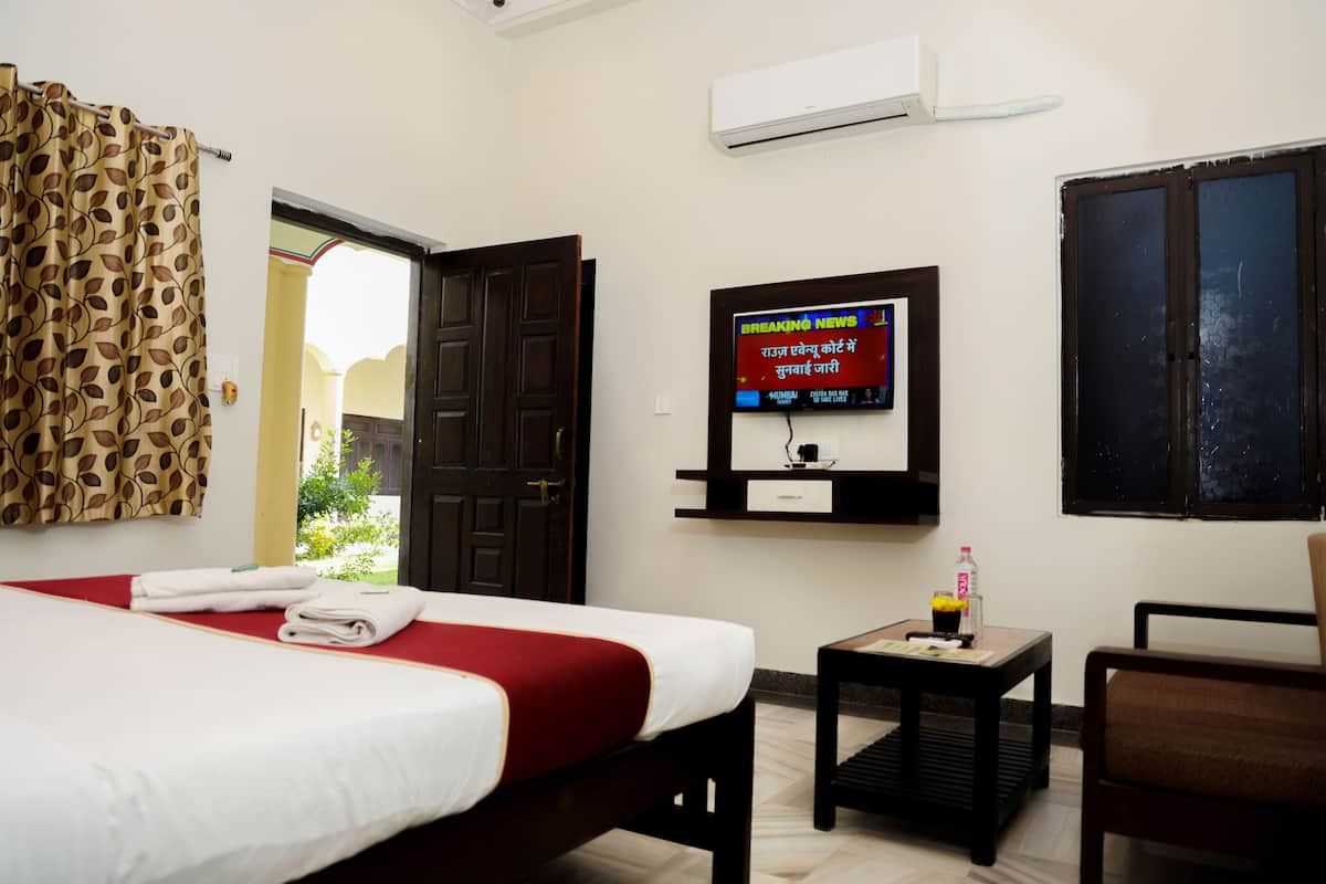 A hotel room with a bed, a TV mounted on the wall, a small table with a bottle and glasses, and a chair.