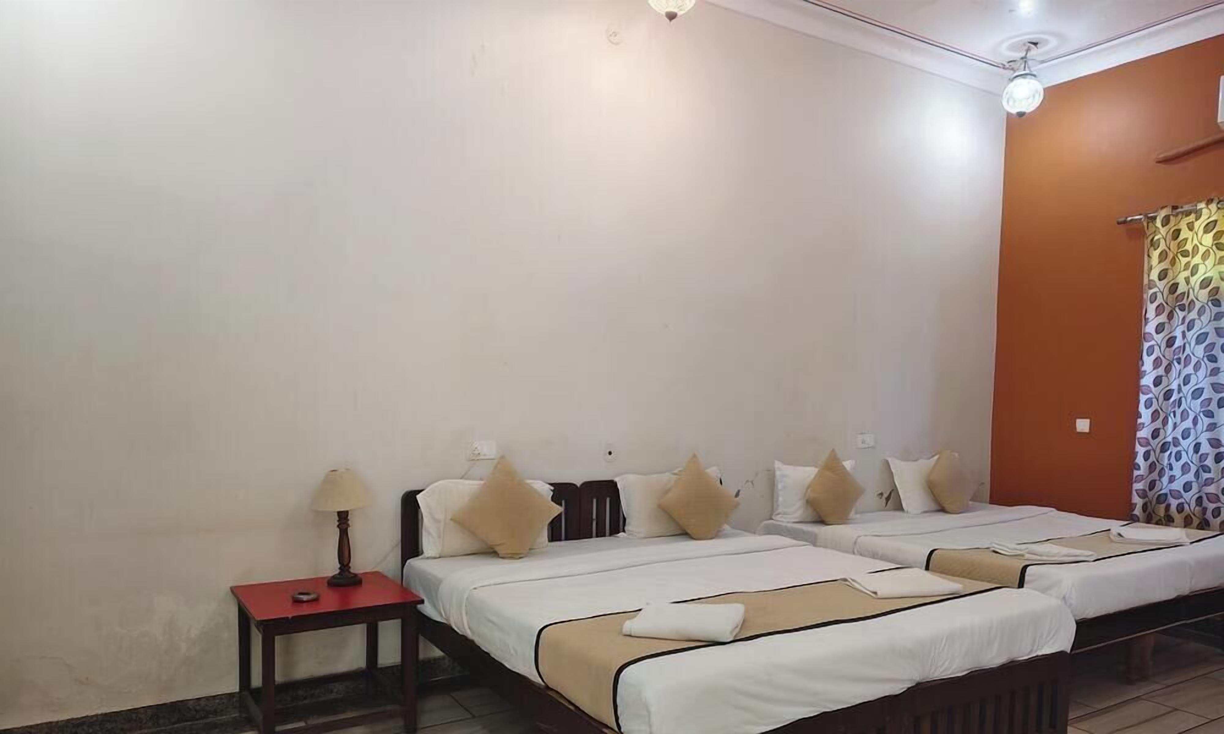 A hotel room with two beds, a nightstand, a lamp, and a patterned curtain.