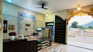 A reception area with a marble floor, a reception desk, a ceiling fan, and a decorative ceiling design. - Hotel Mewad Haveli Pushkar (Pushkar)