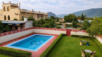 Una piscina con bordo rosso, circondata da un prato curato e qualche sedia.