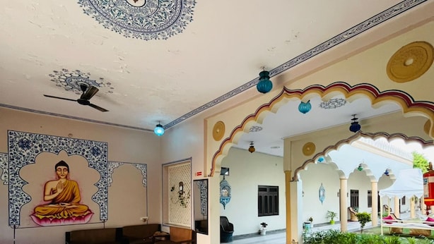 A spacious hall with a marble floor, a Buddha mural, and traditional arches. - Hotel Mewad Haveli Pushkar (Pushkar)