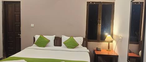 Una cama bien tendida con ropa de cama blanca y verde, una mesita de noche con una lámpara, y una ventana con vista al cielo nocturno.