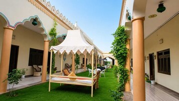 Un patio con una cama con dosel, sillas y plantas en macetas.