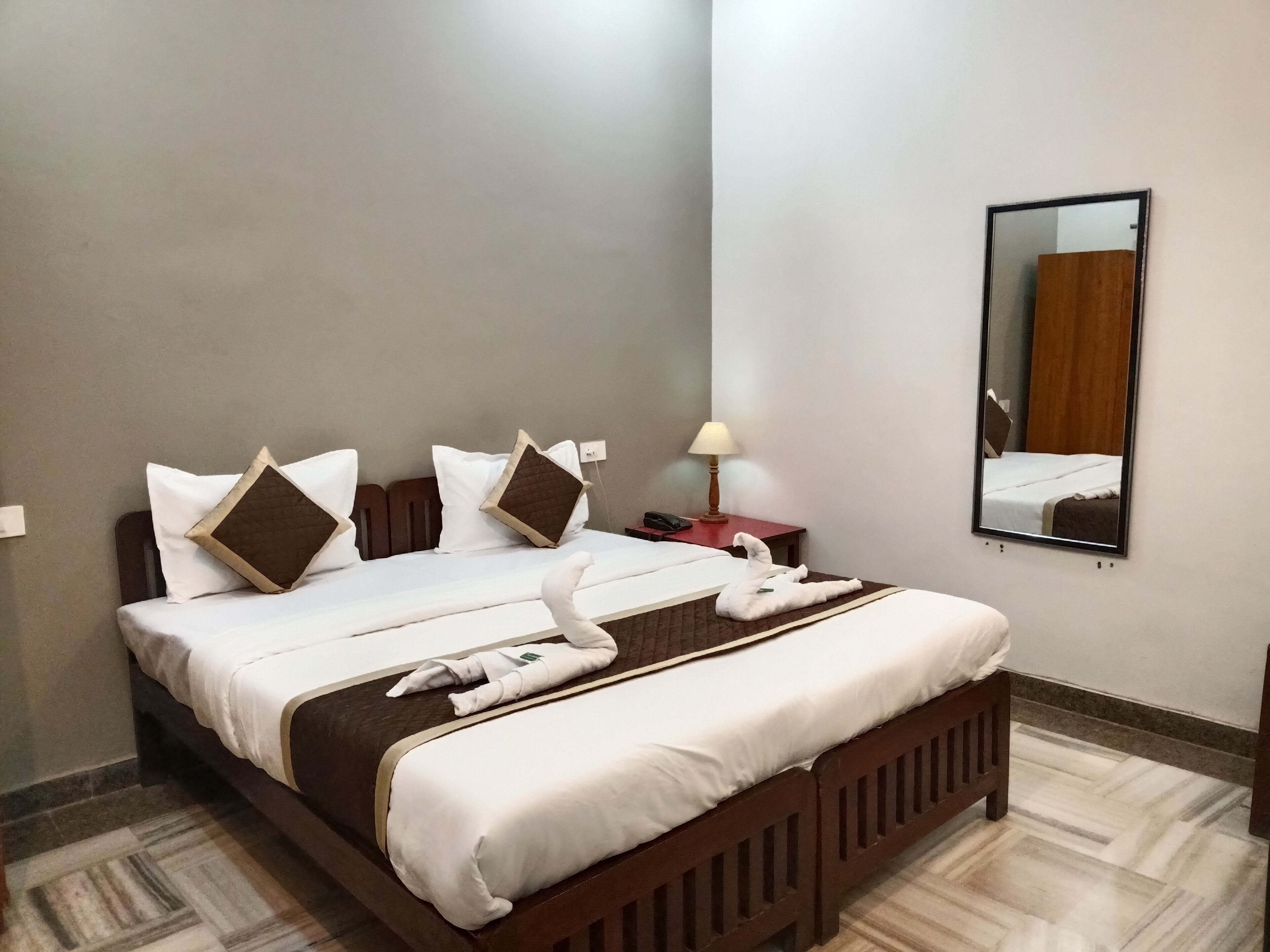 A neatly made bed with white linens and brown pillows, a bedside lamp, and a mirror on the wall.