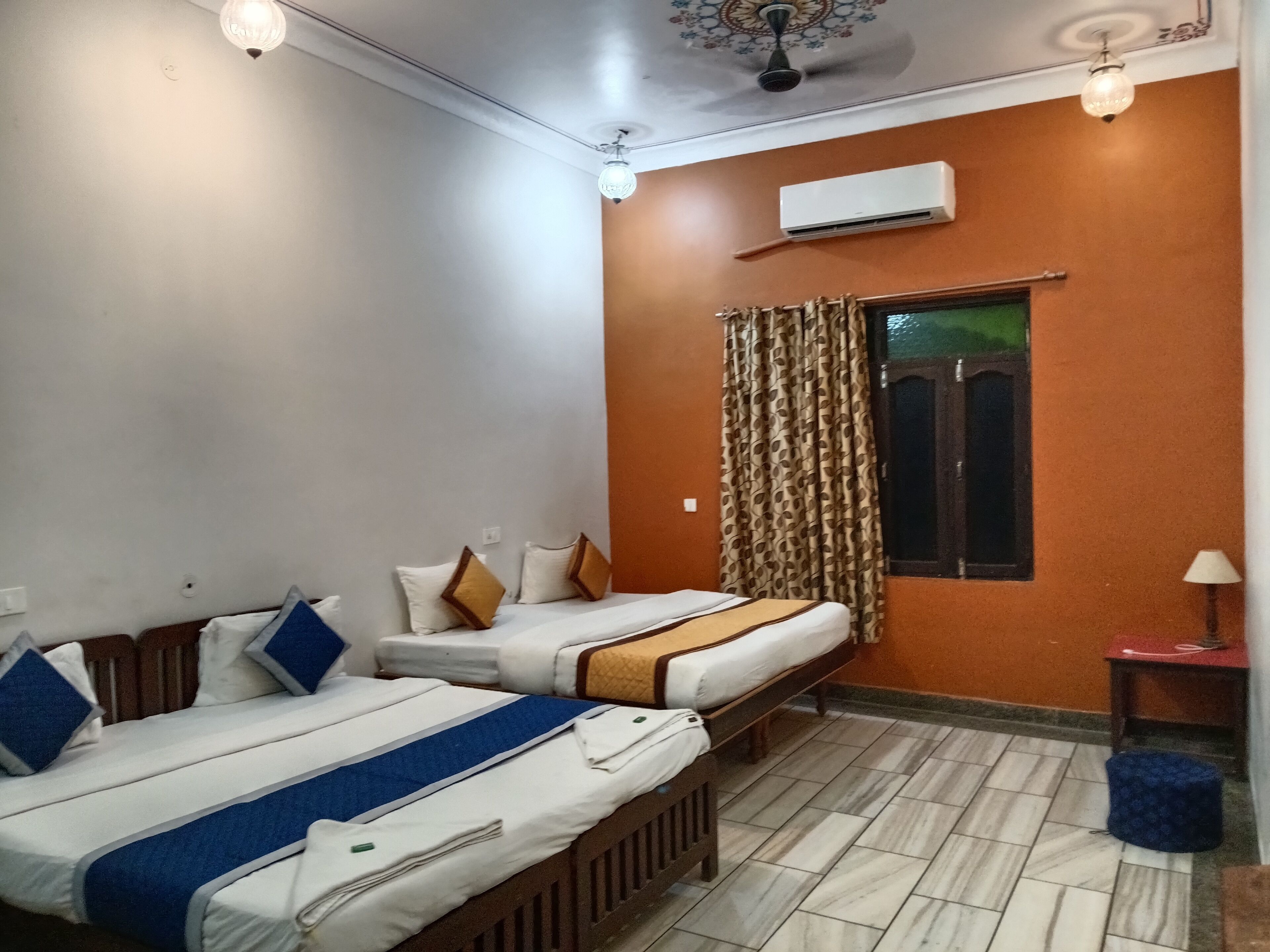 A hotel room with two beds, a window with curtains, an air conditioning unit, and a ceiling fan.
