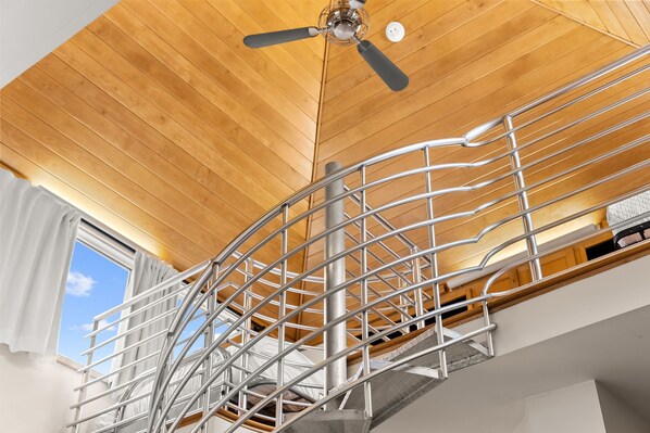 Una escalera de caracol con barandas de metal que conduce a un techo de madera con un ventilador de techo.