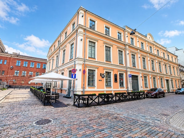 A building with a corner entrance, outdoor seating area, and a cobblestone street.
