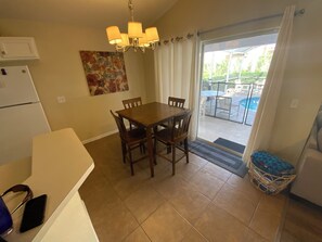 A dining area with a wooden table and chairs, a chandelier, and a view of an outdoor pool through a sliding glass door.