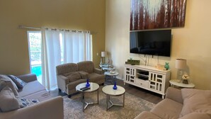 Ein geräumiges Wohnzimmer mit einem großen Fernseher, zwei Sofas, einem Couchtisch und einem Deckenventilator.