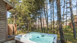 Un bain à remous situé dans un espace boisé, avec une terrasse en bois et une vue sur des maisons au loin.