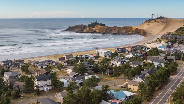 Une zone résidentielle côtière avec des maisons, une plage et un promontoire rocheux visible au loin.