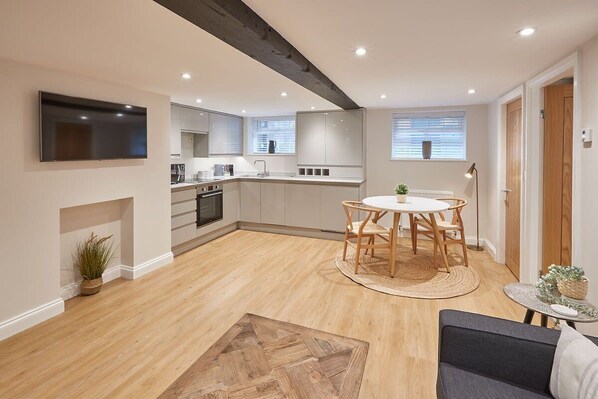 Cozy living space with a kitchen, dining, and seating area, featuring a flat-screen TV and a round dining table.