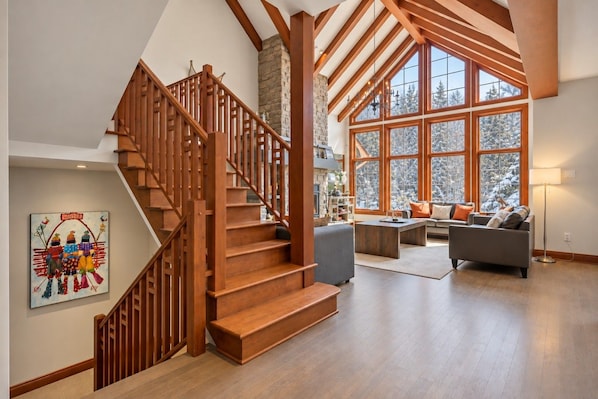 Un vaste espace de vie agrémenté d’un escalier en bois, de grandes fenêtres et d’un coin salon confortable.