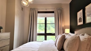 A bedroom with a large bed, a dresser, a window with curtains, and a chandelier.