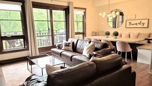 A modern living room with a leather sofa, a glass coffee table, and a dining area with a white table and chairs.