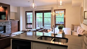 A modern kitchen with a central island, a stone fireplace, and large windows offering a view of the outdoors.