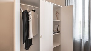 A walk-in closet with hanging clothes and a shelf with books. - Emilia Suite Essence (Modena)