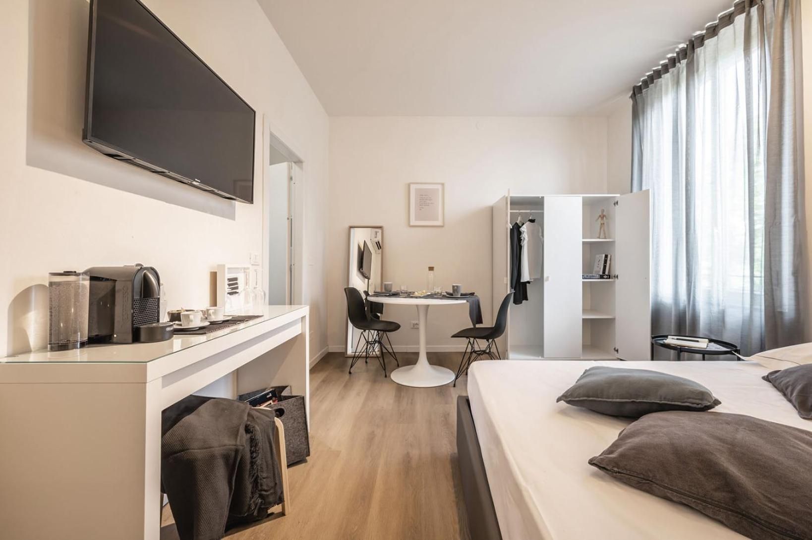 Una camera d'albergo con un letto, una scrivania con una sedia, una televisione, un armadio e una finestra con tende.
